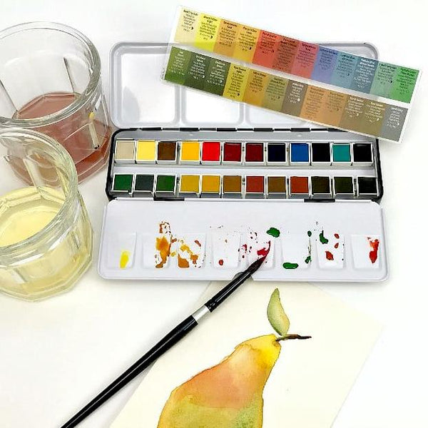 A watercolor paint palette with multiple color wells, a paintbrush, two glass cups of water, and a painted pear on paper, arranged on a white surface.