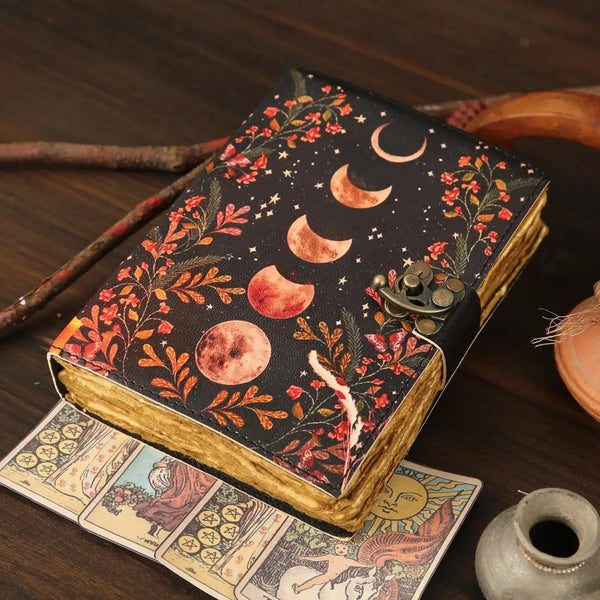 Decorative notebook with moon phases and floral design on a wooden surface with tarot cards.