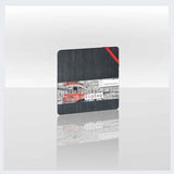 A square black coaster with a printed collage of a red tram and the Polish word 'Zigazń' on a white background, shown on a reflective light gray surface.