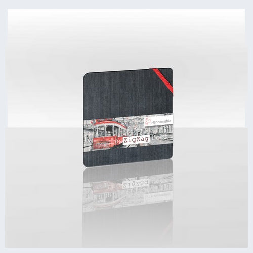 A square black coaster with a printed collage of a red tram and the Polish word 'Zigazń' on a white background, shown on a reflective light gray surface.