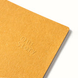 Yellow notebook with 'Our Story' embossed on it against a white background