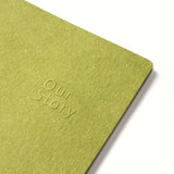 Green notebook with 'Our Story' embossed on the cover against a white background