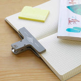 Gray paper clip on a notebook with sticky notes and a magazine.