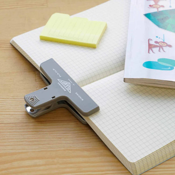 Gray plastic clip on a notebook with sticky notes and a magazine.