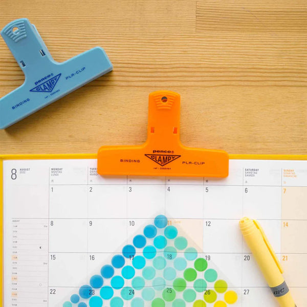 Orange and blue paper clips on a calendar with a yellow pen